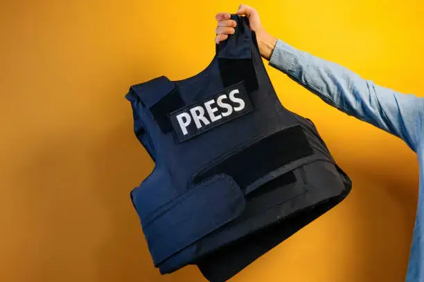 A person holding a bulletproof vest with a PRESS patch on it.